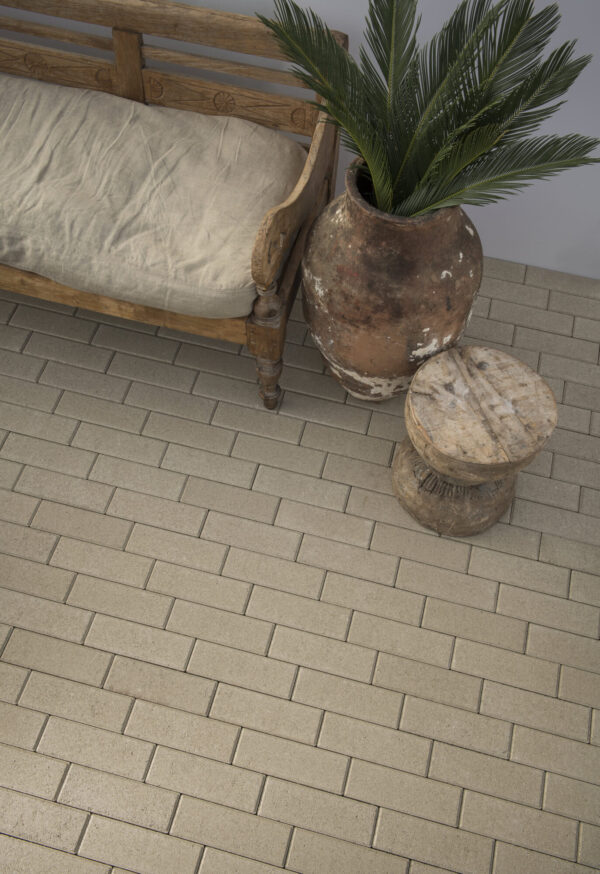 Wooden bench with cushion beside a weathered terracotta urn planted with greenery, on a tan quarter runner paver floor.