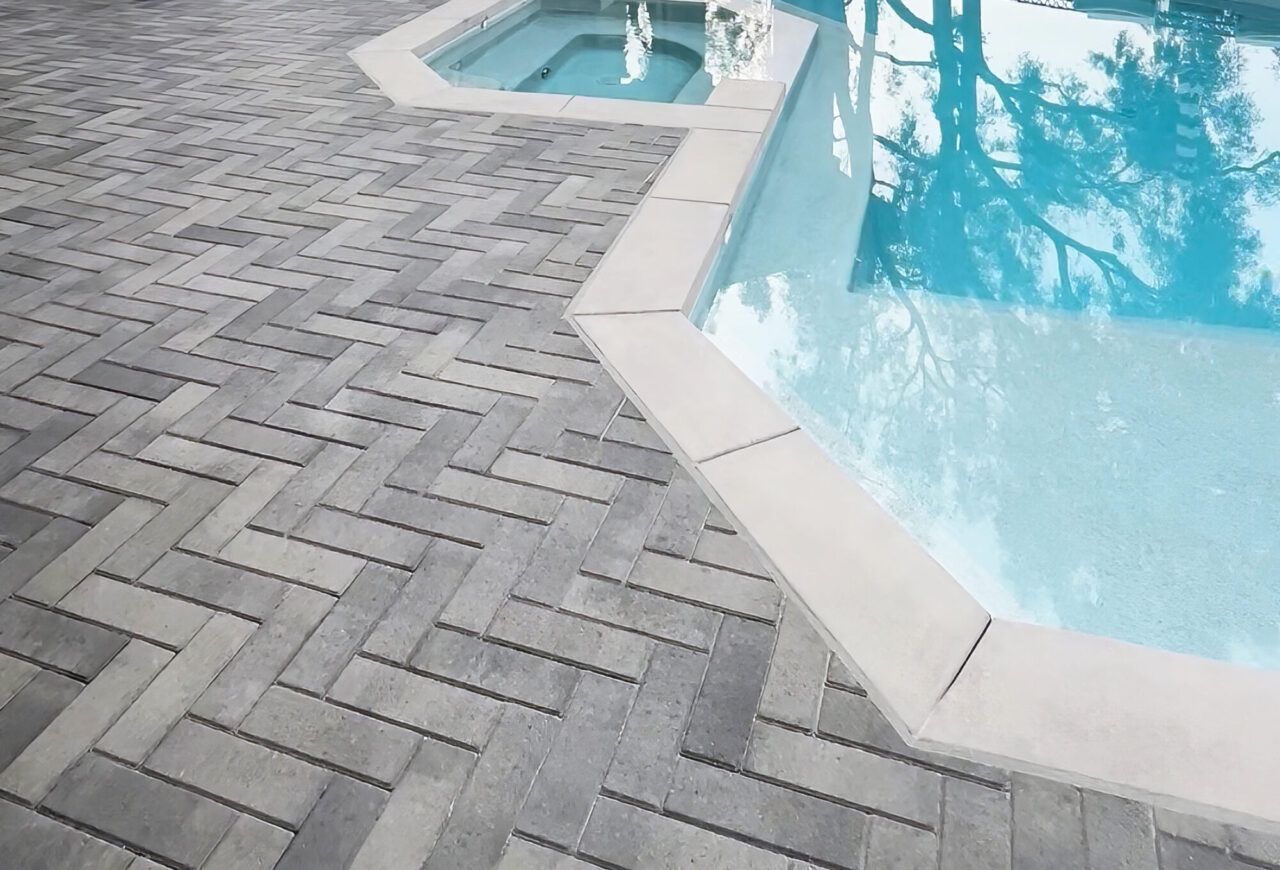 Close up of gray linear pavers on a pool deck beside a pool and spa.