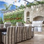 Outdoor dining area with striped slipcovered chairs beside a stone outdoor kitchen with built-in grill and a living green wall.
